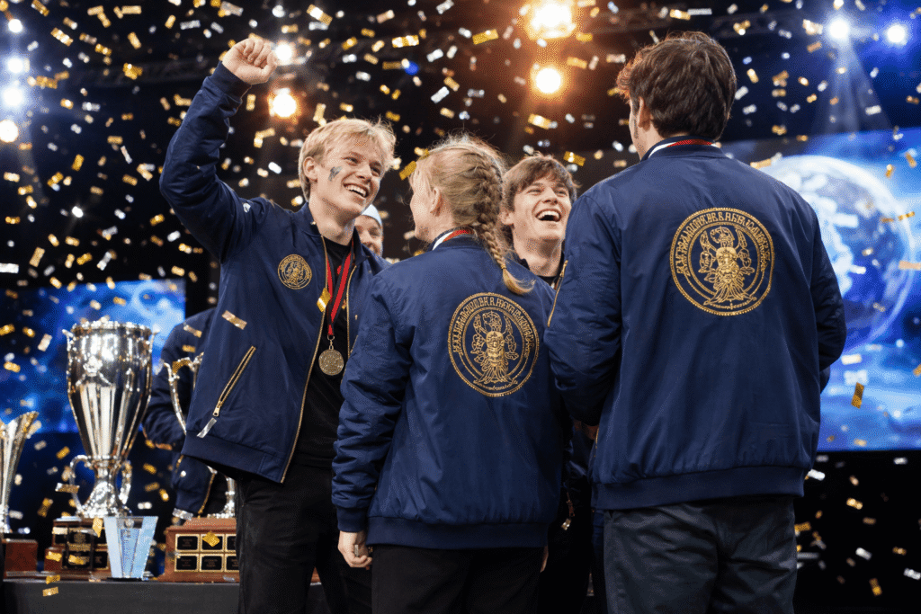 Competition winners in navy blue bomber jackets with gold embroidered logo and back print celebrating on podium with medals and confetti — custom event jackets for competition ceremonies and championship merchandise