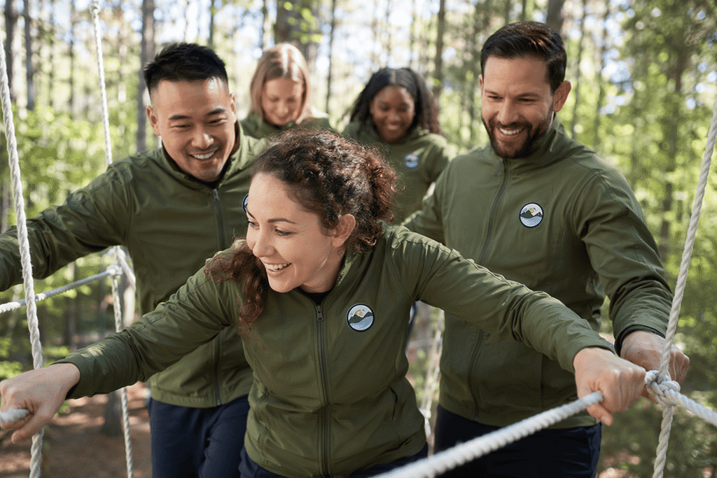 Corporate team in olive green lightweight jackets with embroidered logo patches participating in outdoor team building ropes course — custom team jackets for corporate retreats and team activities